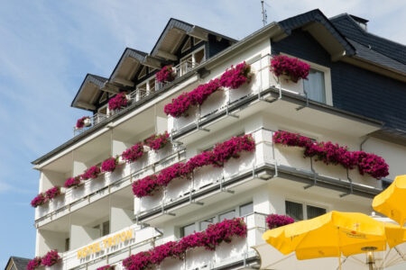 Blick auf das Hotel Triton an einem sonnigen Tag, Blumenkästen sind mit Weinroten Blumen bestückt