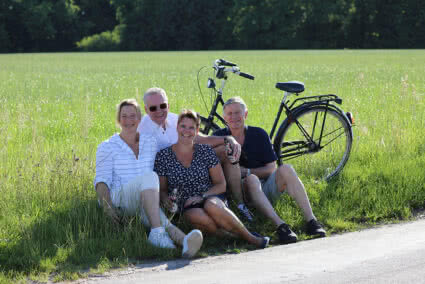 Zwei Paare sitzen mit Bier in der Hand am Straßenrand in einem Feld auf dem ein Fahrrad steht