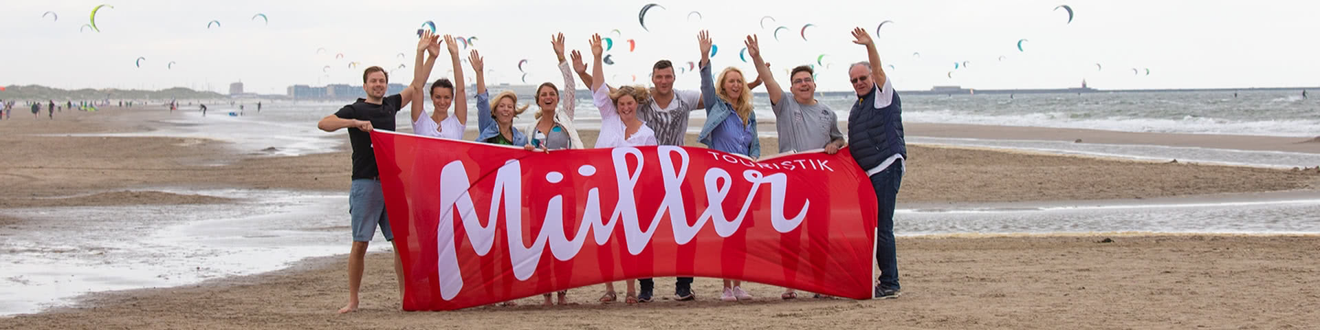 Gruppe steht am Strand in Wijk aan Zee und hält eine Müller-Touristik-Fahne